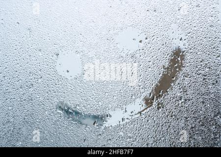 Fröhliches Lächeln, handgezeichnetes Lächeln auf der Oberfläche aus gedämpftem Glas oder Fenster mit Regentropfen an regnerischen Tagen. Hintergrund von Regentropfen auf der Fensterscheibe Stockfoto