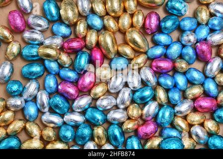 Große & kleine rosa, blau, silber und Gold Folie umwickelt Schokolade ostereier, vor einem hellen Holz Hintergrund. Stockfoto