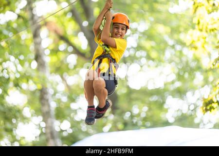 Teenager-Mädchen geht auf Scharnierweg in extreme Seil Park im Sommerwald. Höhenklettertraining des Kindes auf Abenteuerstrecke, ausgestattet mit Stockfoto