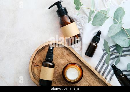 Set aus natürlichen Bio-SPA-Beauty-Produkten auf Holzbrett mit Eukalyptusblättern. Bernsteinfarbene Glas-Kosmetikflaschen, Ansicht von oben. Stockfoto