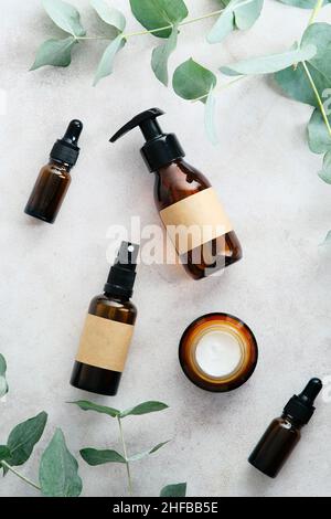 Bernsteinfarbene Glas-Kosmetikflaschen und Eukalyptusblätter auf dem Steintisch von oben. Natürliche Bio-Beauty-Produkte Set. Hautpflegekonzept. Stockfoto
