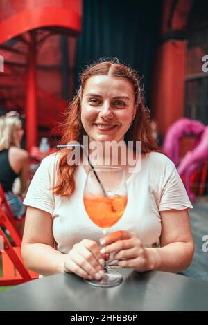 30s Frau ruhen sich aus und genießen Sie mit einem Glas kalten Aperitif Aperol Spritz auf dem Hintergrund des Restaurants. Stockfoto