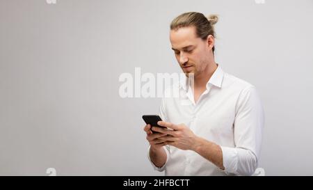 Junge blonde bärtige Mann SMS-Nachricht auf Smartphone über einem weißen Studio-Hintergrund mit Kopieplatz Stockfoto