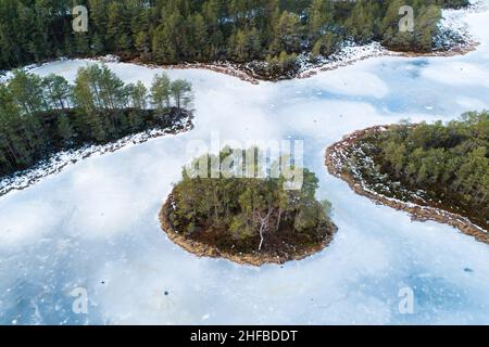 Ein atemberaubender Blick aus der Vogelperspektive auf einen gefrorenen Moorsee mit einer kleinen Insel in estnischer Wildnis. Stockfoto