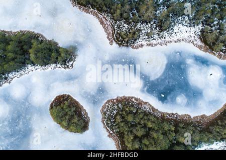 Ein atemberaubender Blick aus der Vogelperspektive auf einen gefrorenen Moorsee mit einer kleinen Insel in estnischer Wildnis. Stockfoto