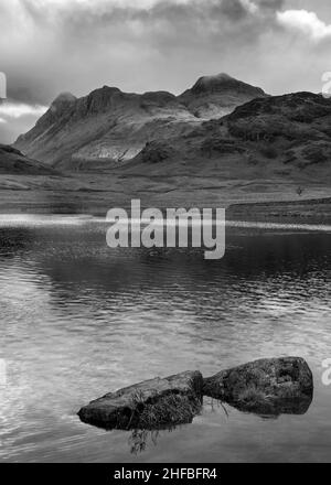 Schwarz-Weiß Epische Landschaft mit Sonnenaufgangslicht über Blea Tarn im Lake District mit atemberaubendem Licht auf fernen Bergen Stockfoto