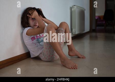 Weinendes Mädchen, das während des COVID 19-Ausbruchs zu Hause auf dem Boden sitzt. Stockfoto