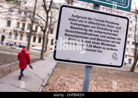 Furth, Deutschland. 15th Januar 2022. 15. Januar 2022, Bayern, Fürth: Eine Frau geht an einem Schild vorbei, auf dem die Abstandsregeln in der Parkordnung aufgeführt sind. Foto: Nicolas Armer/dpa Quelle: dpa picture Alliance/Alamy Live News Stockfoto