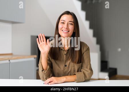 Die junge und energische asiatische frisch-Absolventin ist bereit für ein Online-Interview bei einem Videoanruf, sitzt am Schreibtisch und schaut und winkt der Kamera zu und sagt Hallo. Konzept für die Jobsuche Stockfoto