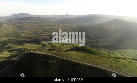 Luftaufnahme von grünen bewaldeten Hügeln und kleinen See auf bewölktem Himmel Hintergrund. Fliegen über Sommerberge mit wachsenden grünen Bäumen. Stockfoto