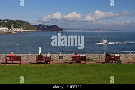 Die Menschen genießen den Meerblick von Shaldon, South Devon, mit Blick auf Teignmouth und den entfernten Hole Head, wenn das Hafenlotsenboot ankommt. Stockfoto