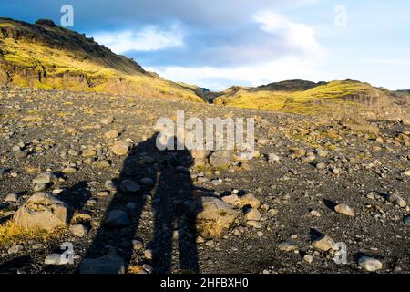 Ein Mann und eine Frau, die die Hände halten, werden mit ihren Schatten, die sich über eine wunderschöne isländische Bergkette mit Felsen, schwarzem Vulkanismus erstrecken, umschwärzt Stockfoto