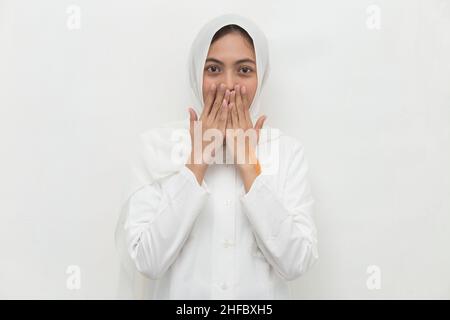 Junge asiatische Frau trägt Hijab schockiert Abdeckung Mund mit Händen für Fehler. Geheimes Konzept. Stockfoto