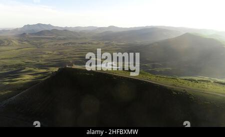 Luftaufnahme von grünen bewaldeten Hügeln und kleinen See auf bewölktem Himmel Hintergrund. Fliegen über Sommerberge mit wachsenden grünen Bäumen. Stockfoto