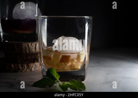 Zwei Gläser Fileld mit Glühwein infundiert Gin Rum Wodka mit Eiskugeln, Scheiben von Apfelfrüchten und Blätter von Minze zeigen das Hobby des Mullings für Stockfoto