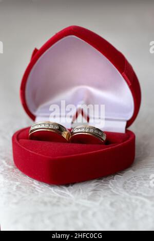 Zwei goldene Ringe aus Weiß- und Gelbgold liegen in einer Schachtel in Form eines Herzens aus rotem Samt Stockfoto