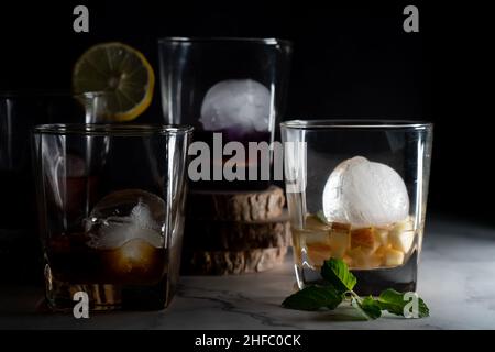 Mehrere Whiskey-Gläser gefüllt mit verschiedenen farbigen infundierten Glühwein Gin Rum Wodka Getränke mit Eisbällen und Keile aus Limone, Minze zeigt die Stockfoto
