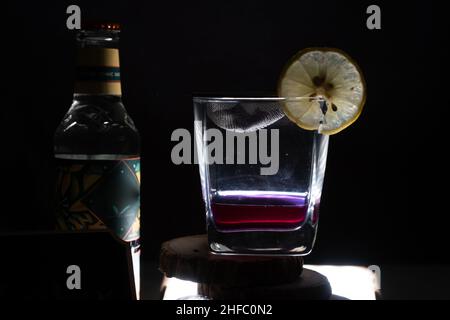 Auf schwarzem Hintergrund gedrehtes Licht mit Glasfilet mit Glühwein-Gin mit Zitronenkeil und einer Flasche Tonic an der Seite für eine Feier Stockfoto