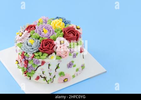 Hausgemachter Kuchen mit schönen Blumen auf blauem Hintergrund dekoriert, minimalistisches Kuchenkonzept Stockfoto