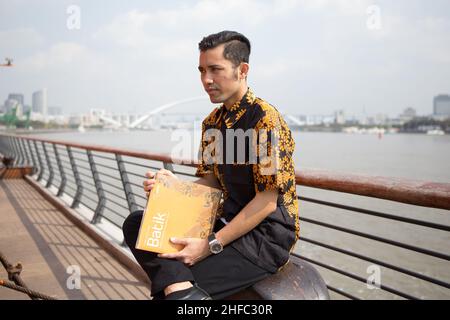 Ein junges männliches Model in indonesischer Batik liest im Long Museum ein Buch mit dem Titel Batik vor dem Hintergrund des Huangpu-Flusses und der Lupu-Brücke Stockfoto