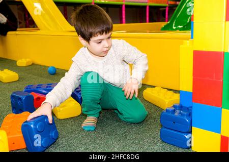 Ein Vorschuljunge spielt mit großen Baublöcken im Spielzimmer, einem Kinderanimationszentrum und einem Indoor-Spielplatz. Stockfoto