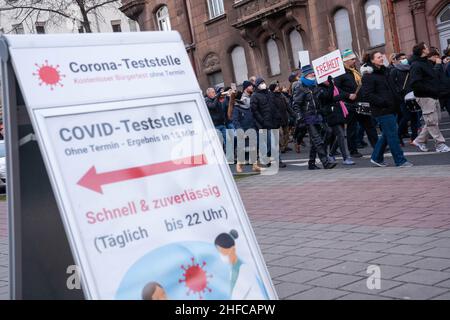 Furth, Deutschland. 15th Januar 2022. 15. Januar 2022, Bayern, Fürth: Teilnehmer einer Demonstration gegen Corona-Maßnahmen gehen an einem Schild vorbei, das auf einen Corona-Testplatz hinweist. Foto: Stringer/dpa Kredit: dpa picture Alliance/Alamy Live News Stockfoto