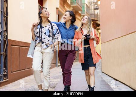 Glückliche multirassische weibliche beste Freunde, die während der Ferien in der Stadt spazieren gehen Stockfoto