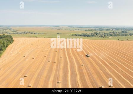 Hay-Ballen mit Hay-Ballenpresse mit Landmaschinen erstellen. Traktor mit Heupresse arbeitet auf gelbem Feld gesammelte Heuballen: Luftdrohnenaufnahme. Stockfoto