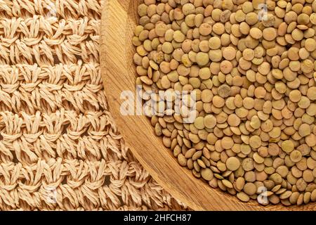 Ungekochte grüne Bio-Linsen in einer Holzplatte auf einer Strohmatte, Makro, Draufsicht. Stockfoto