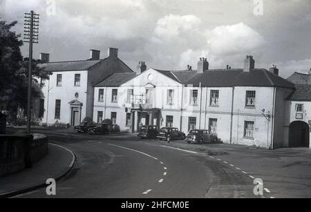 1950s, Autos der Ära, die vor dem Croft Spa Hotel, Croft on Tees, Darlington, Yorkshire, England, Großbritannien und die Great North Road, die A167. Ein kleines Hotel wurde 1808 erbaut, um Besucher zu versorgen, die wegen der im Dorf angebotenen Kurbäder kamen, und 1835 wurde der Architekt der Kathedrale von Durham, Ignatius Bonomi, für die Planung und Erweiterung des Hotels eingesetzt. Auf der linken Seite befindet sich der Ballsaal, der 1860 hinzugefügt wurde, als er von Thomas Winteringham geleitet wurde, der aus den Ställen auch ein Gestüt im Hotel führt. Diese wurden zu Werkstätten und einer Garage. Nicht im Bild zu sehen, aber rechts ist die St. Peter Kirche. Stockfoto