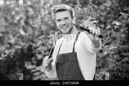 Werkzeuge zum Braten von Fleisch im Freien. Grillparty. Burger kochen. Picknick-Konzept. BBQ-Koch. Ein hübscher Kerl, der Essen kocht. Mann hält Grillausrüstung Stockfoto