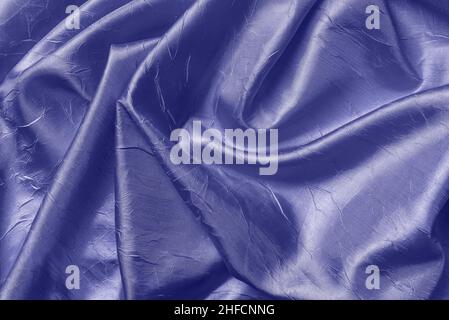 Blauviolette Textur aus drapierter, glänzender, faltiger Seide. Hintergrund aus gefaltetem Satinstoff in trendiger Farbe des Jahres 2022 sehr peri. Zerknitterte Qualität. Stockfoto