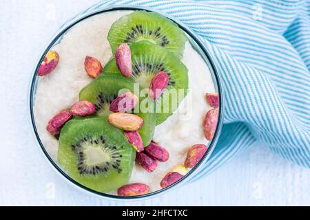 Pudding Dessert, hausgemachter Vanillepudding oder Joghurt mit Kiwi-Früchten und Pistazien auf dem Tisch. Draufsicht Schüssel Joghurt mit Früchten zum Frühstück Stockfoto