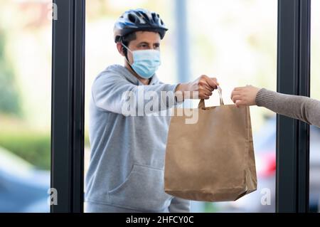 Aufnahme eines maskierten Mannes, der zu Hause ein Lebensmittelpaket mit Fokus auf die Hand- und Kopierfläche liefert Stockfoto