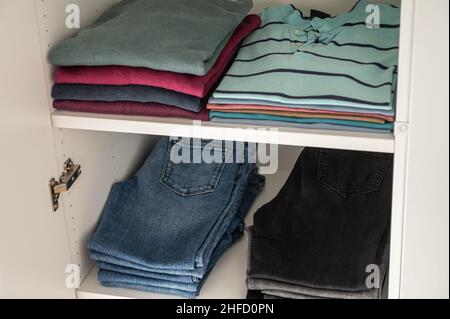 Ordentlich gefaltete Pullover und Jeans und andere Kleidung auf Regalen im Kleiderschrank Stockfoto