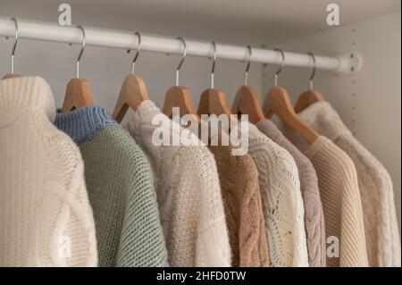 Warmer Winterpullover aus beigefarbener Wolle und Strickmode, die im Kleiderschrank hängen Stockfoto