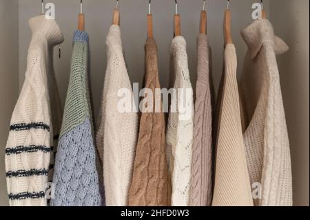 Warmer Winterpullover aus beigefarbener Wolle und Strickmode, die im Kleiderschrank hängen Stockfoto