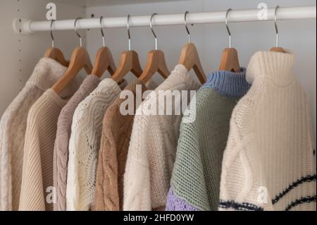 Warmer Winterpullover aus beigefarbener Wolle und Strickmode, die im Kleiderschrank hängen Stockfoto