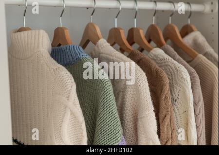 Warmer Winterpullover aus beigefarbener Wolle und Strickmode, die im Kleiderschrank hängen Stockfoto