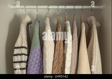 Warmer Winterpullover aus beigefarbener Wolle und Strickmode, die im Kleiderschrank hängen Stockfoto