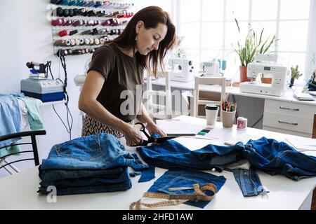 Kreislaufwirtschaft. Nachhaltige Mode. Wiederverwendung, Reparatur, Upcycle. Denim Upcycling Ideen, Reparatur und Verwendung von alten Jeans. Frau Schneiderin reparieren alten Denim Stockfoto