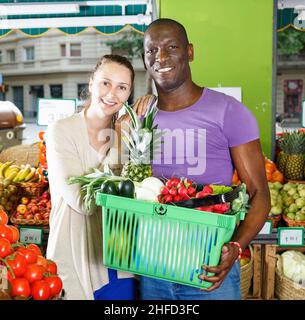 Mann und Frau wählen Produkte mit Korb auf dem Obstmarkt. Stockfoto