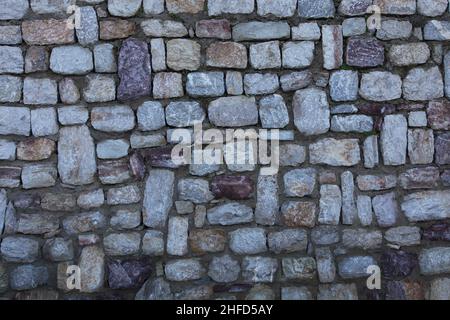 Steinwall Hintergrund. Eine alte handgefertigte Steinwand. Es werden asymmetrische Steine verwendet. Nahaufnahme. Stockfoto
