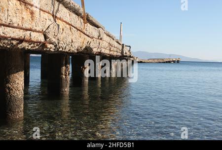 Ein alter Seebrücke. Abgenutzt und veraltet. Der Beton des Piers gießt und die Bars sind verrostet. Stockfoto