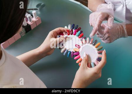 Schönheitssalon. Master zusammen mit dem Kunden, wählt Farbe der Gelpolitur in Maniküre Raum. Master wählt zusammen mit dem Kunden die Farbe der Gelpolitur. Legen Sie verschiedene Farben von Nagellack auf Palette. Stockfoto