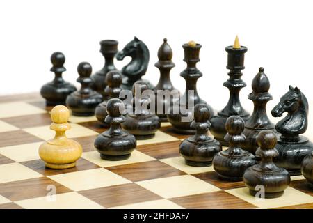 Einer der weißen Schachfiguren greift schwarze Schachfiguren-Armee an. Hölzerne Schachfiguren auf dem Brett. Schachspiel-Position. Stockfoto