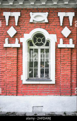 Das Fenster eines alten Backsteingebäudes ist wunderschön mit Flachreliefs dekoriert. Außenansicht des alten Backsteinhauses. Stockfoto