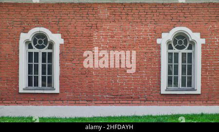 Zwei Fenster in einer Reihe auf der Ziegelwand des alten Hauses. Fassade eines alten Gebäudes. Stockfoto