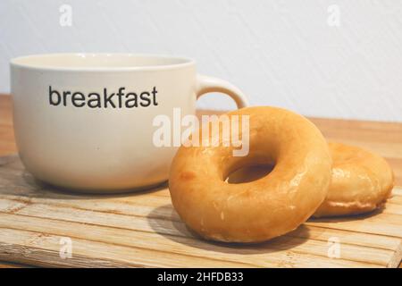 Zwei klassische süße Donuts und eine Tasse Tee oder Kaffee auf einem Holzständer. Image des Frühstückskonzepts. Stockfoto