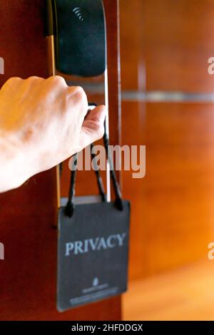 Die Tür wurde von Hand geöffnet und der Türgriff mit dem Schild „Privacy“ hing an der geschlossenen Tür des Hotelzimmers. Konzept-Privatsphäre, Sicherheit, Gastfreundschaft, Reisen. Stockfoto